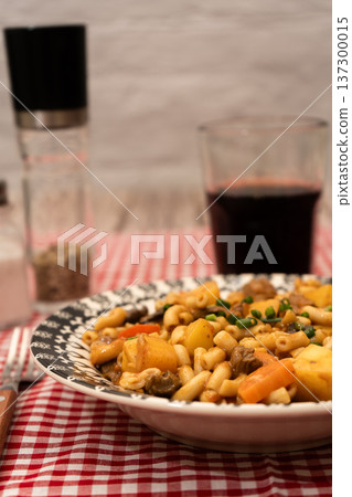 Rustic noodles stew with meat and vegetables on a checkered tablecloth Rustic noodles stew with meat and vegetables on a checkered tablecloth 137300015