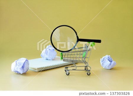 Magnifying glass on shopping cart and crumpled paper around. Magnifying glass on shopping cart and crumpled paper around. 137303826