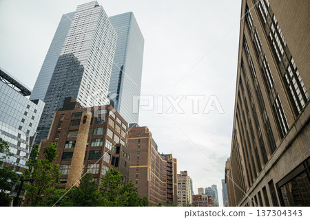 A modern glass skyscraper rises above historic brick buildings in Manhattan, New York City. The urban skyline reflects architectural contrast and real estate development. A modern glass skyscraper rises above historic brick buildings in Manhattan, New York City. The urban skyline reflects architectural contrast and real estate development. 137304343