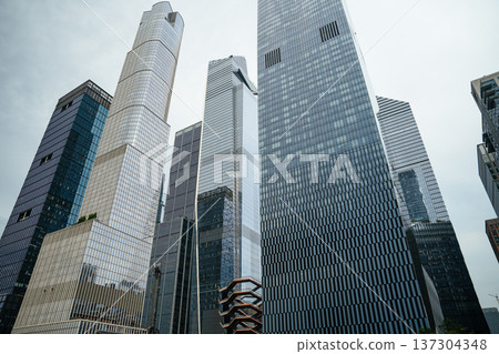 A dramatic low angle perspective highlights towering glass skyscrapers in Manhattan, New York City. The modern financial district architecture reflects urban development and corporate power. A dramatic low angle perspective highlights towering glass skyscrapers in Manhattan, New York City. The modern financial district architecture reflects urban development and corporate power. 137304348
