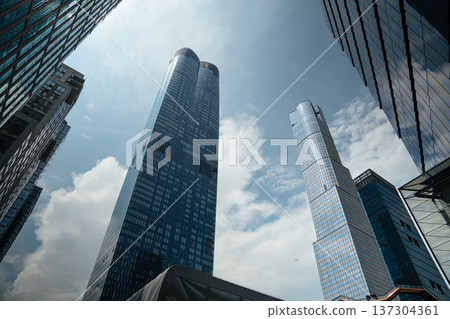 Reflective glass skyscrapers rise dramatically toward a bright cloudy sky in Manhattan, New York City. Modern urban architecture creates a powerful vertical skyline composition. 137304361