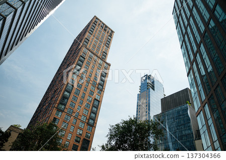 Brick residential tower and modern glass skyscrapers rising against the sky in Manhattan, New York City. Urban architecture highlights the contrast between classic and contemporary design. Brick residential tower and modern glass skyscrapers rising against the sky in Manhattan, New York City. Urban architecture highlights the contrast between classic and contemporary design. 137304366