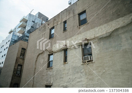 Weathered exterior wall of an older Manhattan residential building shows peeling texture and a window air conditioner. Historic urban housing details illustrate everyday New York City architecture. 137304386