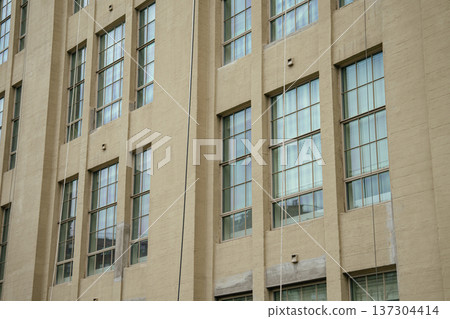 A vertical view of a beige architectural facade shows repeating tall windows on a Manhattan building. The clean geometric pattern highlights modern urban design and city structure in New York. A vertical view of a beige architectural facade shows repeating tall windows on a Manhattan building. The clean geometric pattern highlights modern urban design and city structure in New York. 137304414