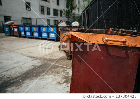 Large metal dumpsters and blue recycling containers line a fenced city service area. The scene illustrates waste management, sanitation infrastructure, and environmental responsibility. Large metal dumpsters and blue recycling containers line a fenced city service area. The scene illustrates waste management, sanitation infrastructure, and environmental responsibility. 137304425