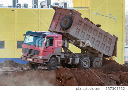 A red dump truck unloads soil at a construction site in winter 137305332