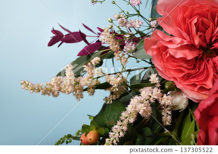 Close up of floral bouquet with pink roses, white astilbe, and hypericum berries against a light blue background. Close up of floral bouquet with pink roses, white astilbe, and hypericum berries against a light blue background. 137305522