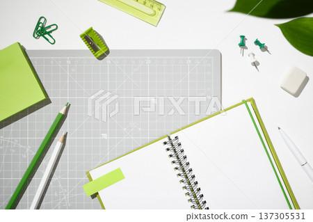 Flat lay of green stationery, open spiral notebook, and cutting mat on white background. Workspace organization for creative projects with copyspace 137305531