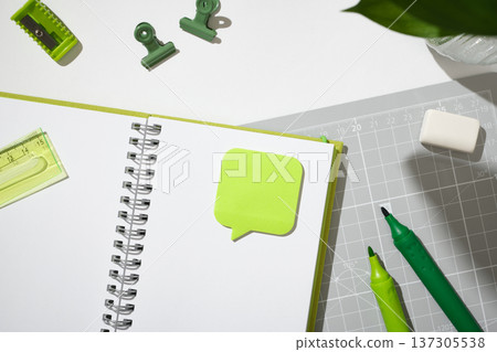 Open spiral notebook with a green speech bubble sticky note on a grey cutting mat. Copyspace Open spiral notebook with a green speech bubble sticky note on a grey cutting mat. Copyspace 137305538