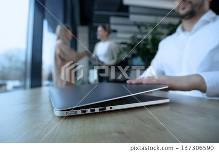 A man is sitting at a desk with a laptop open in front of him A man is sitting at a desk with a laptop open in front of him 137306590