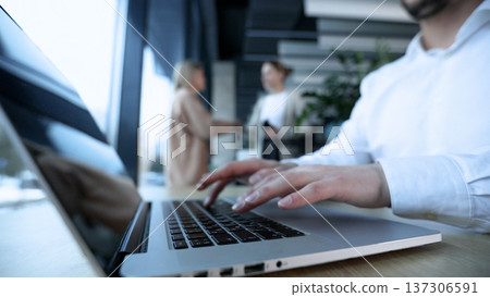 A man is typing on a laptop in front of a window A man is typing on a laptop in front of a window 137306591