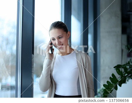 A woman is talking on her cell phone while smiling A woman is talking on her cell phone while smiling 137306656