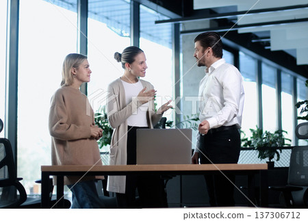 Three people are standing around a desk in a business setting Three people are standing around a desk in a business setting 137306712