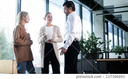 Three people are standing in a room, one of them is wearing a brown sweater 137306891