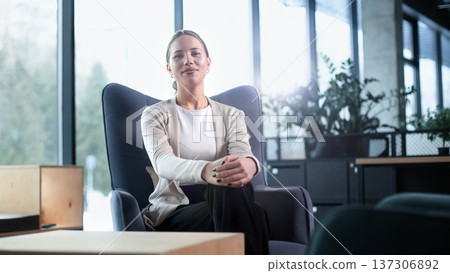 A woman sits in a chair in a room with a potted plant in front of her A woman sits in a chair in a room with a potted plant in front of her 137306892