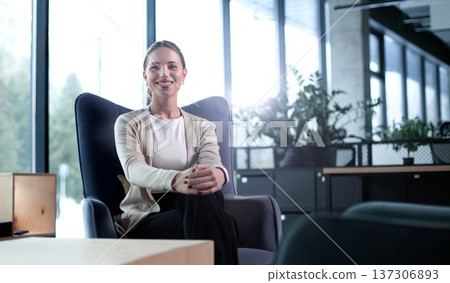 A woman sits in a chair in a room with a potted plant in front of her A woman sits in a chair in a room with a potted plant in front of her 137306893