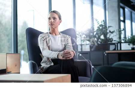 A woman sits in a chair in a room with a potted plant in front of her A woman sits in a chair in a room with a potted plant in front of her 137306894