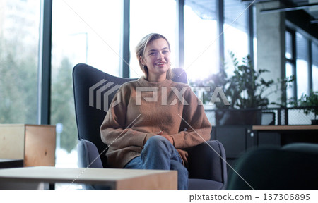 A woman is sitting in a chair in a room with a potted plant in front of her 137306895