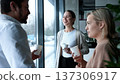 Three people are standing in front of a window, smiling and holding cups 137306917