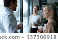 Three people are standing in front of a window, smiling and holding cups 137306918