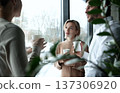 Three people are standing in front of a window, smiling and holding cups 137306920