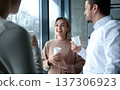 Three people are standing in front of a window, smiling and holding cups 137306923