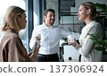 Three people are standing in front of a window, smiling and holding cups 137306924