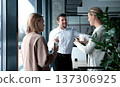 Three people are standing in front of a window, smiling and holding cups 137306925