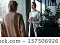 Two women are talking in a room with a potted plant in the background 137306926