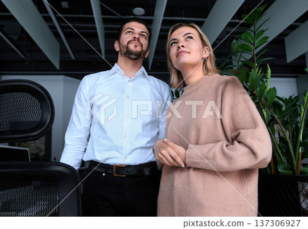 A man and a woman are standing in front of a plant A man and a woman are standing in front of a plant 137306927