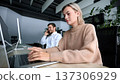 A woman is typing on a laptop while a man talks on the phone 137306929
