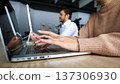 A woman is typing on a laptop while a man looks on 137306930