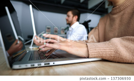 A woman is typing on a laptop while a man looks on A woman is typing on a laptop while a man looks on 137306930