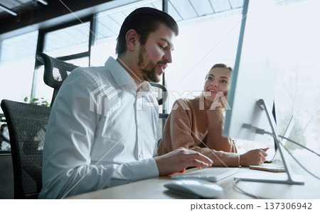 A man and a woman are looking at a computer monitor A man and a woman are looking at a computer monitor 137306942