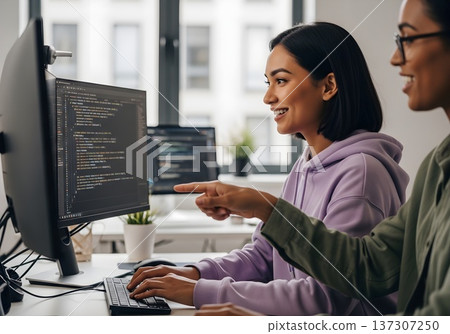 Smiling Female Software Developers Collaborating on Code in a Modern Tech Office Environment 137307250