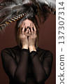 Woman covering face with hands and feather headdress 137307314