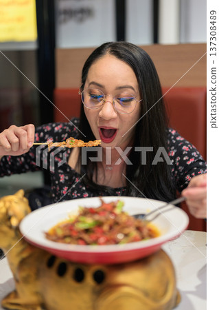 Excited Happy Woman Tasting Spicy Chinese Asian Food in Modern Restaurant 137308489