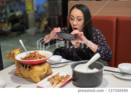 Happy Asian Woman Photographing Spicy Chinese Dish with Smartphone in Restaurant Happy Asian Woman Photographing Spicy Chinese Dish with Smartphone in Restaurant 137308490
