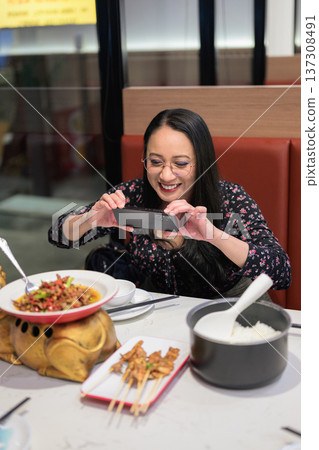 Happy Asian Woman Photographing Spicy Chinese Dish with Smartphone in Restaurant 137308491