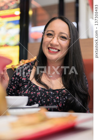 Smiling Woman Eating Grilled Skewer in Asian Restaurant Smiling Woman Eating Grilled Skewer in Asian Restaurant 137308493