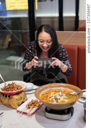 Happy Asian Woman Photographing Spicy Chinese Dish with Smartphone in Restaurant Happy Asian Woman Photographing Spicy Chinese Dish with Smartphone in Restaurant 137308497