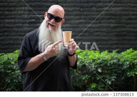 Happy Bearded Bald Man Pointing at Coffee Cup Outdoors Happy Bearded Bald Man Pointing at Coffee Cup Outdoors 137308613
