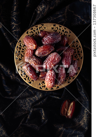 Dates fruits in a golden bowl on black fabric with gold ornamentation. 137308667