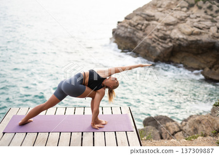 Young woman finding balance and strength in an outdoor yoga session on a wooden deck overlooking the tranquil sea Young woman finding balance and strength in an outdoor yoga session on a wooden deck overlooking the tranquil sea 137309887