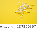 Cotton swabs, also known as q-tips or ear sticks, scattered on a bright yellow background representing personal hygiene and medical care 137309897