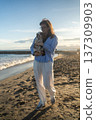 Woman holding a puppy, walking on a sandy beach as the sun sets, enjoying pet ownership and peaceful leisure time 137309903