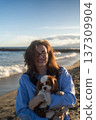 A young woman hugs her Cavalier King Charles Spaniel on the beach at sunset. Warm light, waves, and smiles capture a peaceful, joyful moment of connection and relaxation. 137309904