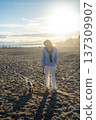 Woman and a small puppy walking on a sandy beach during sunset, enjoying leisure and pet companionship 137309907