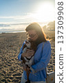 Woman holding and kissing her small pet dog, a cavalier king charles spaniel, enjoying a bond on the beach 137309908