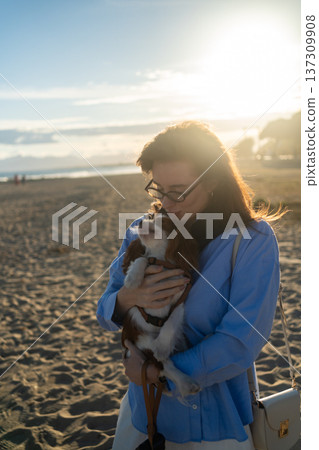 Woman holding and kissing her small pet dog, a cavalier king charles spaniel, enjoying a bond on the beach 137309908